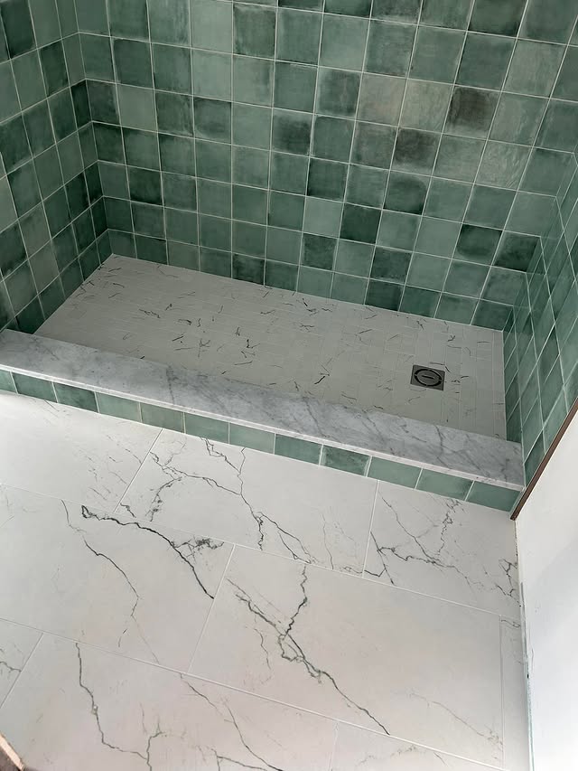 Bath with green zellige-style tile shower and marble floor